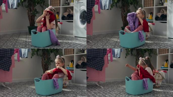 六岁长发女孩坐在蓝色的洗衣碗里。她掏出洗干净的衣服，闻了闻。它闻起来又好又新鲜。洗过的衣服挂在一边。