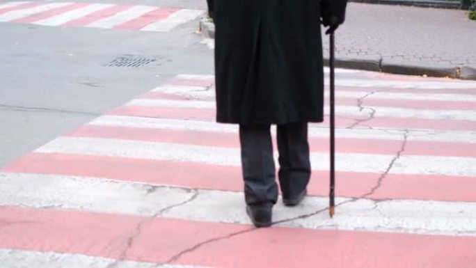 一名视力受损的老人正沿着人行横道缓慢移动。腿和脚的视图