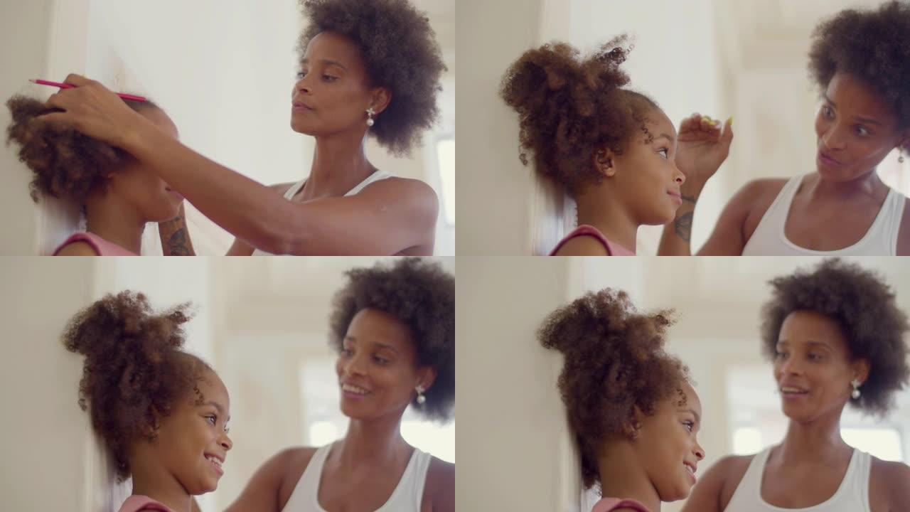 快乐的黑人妇女在墙上测量女儿的身高。
