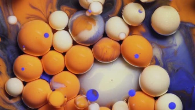 特写多色蓝色橙色和白色油漆气泡在宇宙色彩表面破裂，并在抽象设计中混合。金色闪闪发光的颗粒，墨球滴