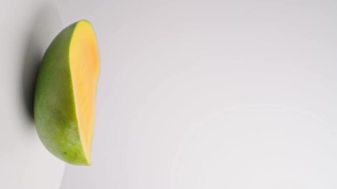 成熟多汁的甜黄色芒果旋转白色背景特写。夏季热带水果，健康食品，芒果汁，有机芒果。芒果切成薄片。4k垂