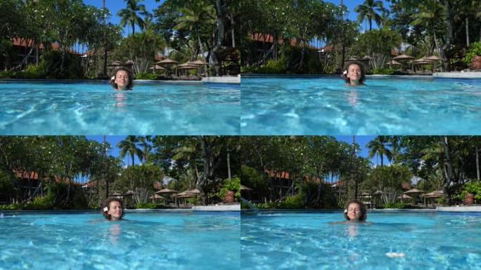 梦想旅行目的地。一位美丽的白人妇女喜欢独自在五星级酒店的清水池中游泳。她把脸暴露在阳光下，晒得漂漂亮
