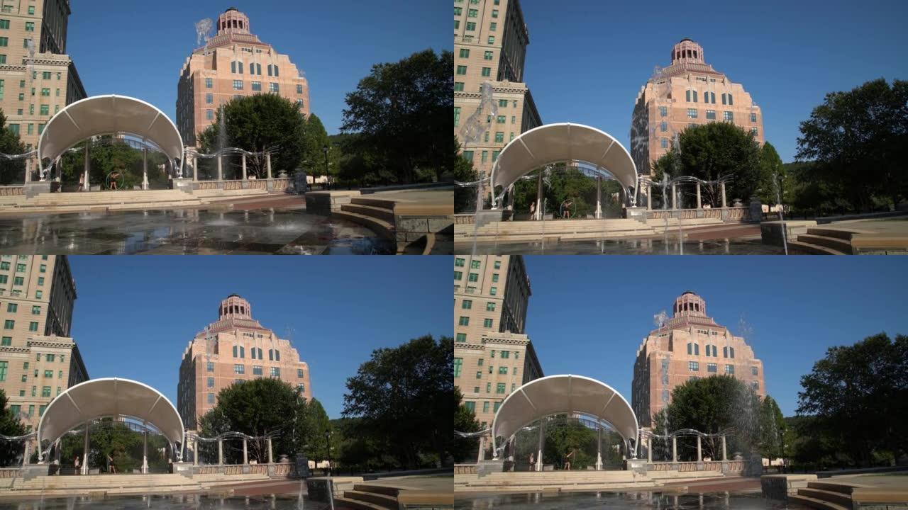 夏天日落时，从北卡罗来纳州阿什维尔市中心帕克广场公园的喷泉看到标志性的阿什维尔市政厅建筑的低角度视图