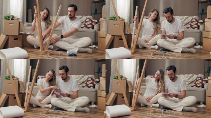快乐的父亲与母亲妻子和丈夫用家具装饰物业空间试图组装新的木制落地灯坐在现代新公寓的地板上移动过程纸箱