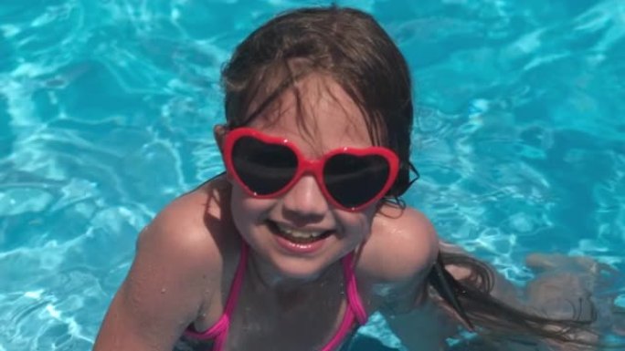 夏天阳光明媚的时候，游泳池里戴着红色心形太阳镜的小女孩