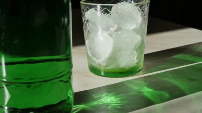 桌子上是一瓶饮料和一杯绿色的玻璃，上面放着被明亮的太阳照亮的冰块，并在桌子上形成尖锐的阴影。多莉·格