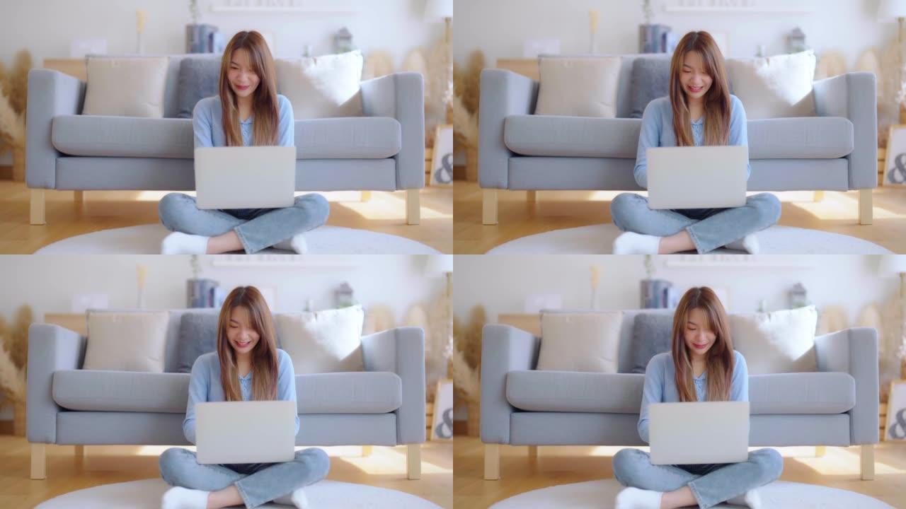 年轻的亚洲女性精神振奋，坐在靠近沙发的地板上，在家用笔记本电脑工作