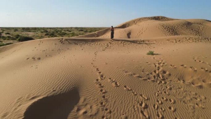 无人机的鸟瞰图。夏天，在阿斯特拉罕 (Astrakhan)，穿着长豹子连衣裙的女人沿着沙漠中的高沙丘