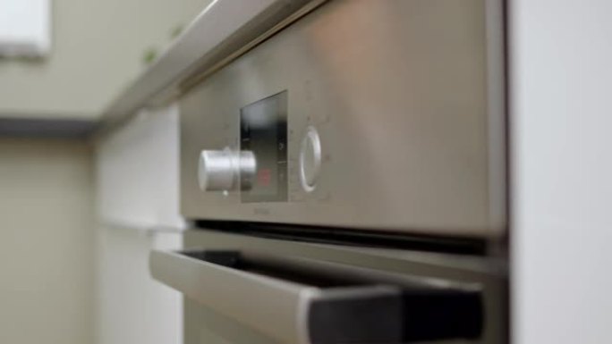 厨师或家庭主妇启动烤箱，并将温度设置为180摄氏度。在灰色金属烤箱中在家烹饪的过程。打开电烤箱。侧视
