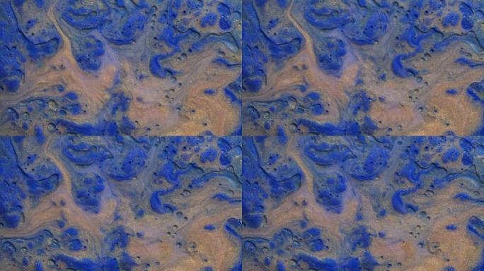 彩色的金粉和丙烯酸涂料散布在蓝色水彩表面上，以奇妙的设计和图案混合在一起。闪闪发光的金色颗粒、墨滴和