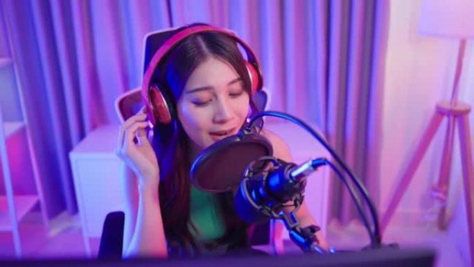 亚洲迷人的音频DJ女人对着麦克风说话。年轻漂亮的女性博客影响者戴着耳机，为家庭广播电台录制早间新闻播