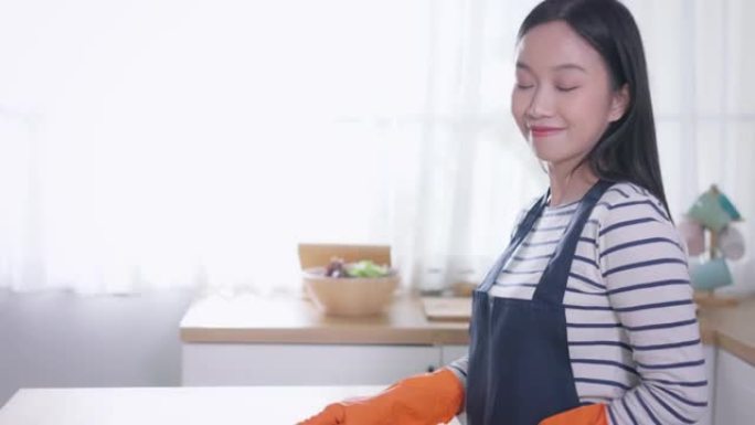 年轻的亚洲妇女看着相机，用除尘器打扫家。漂亮的清洁服务工人家政和整理厨房。家务和家务概念