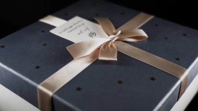 盒子里的礼物，上面系着一条带蝴蝶结的金色丝带，一条信息在黑色背景上旋转