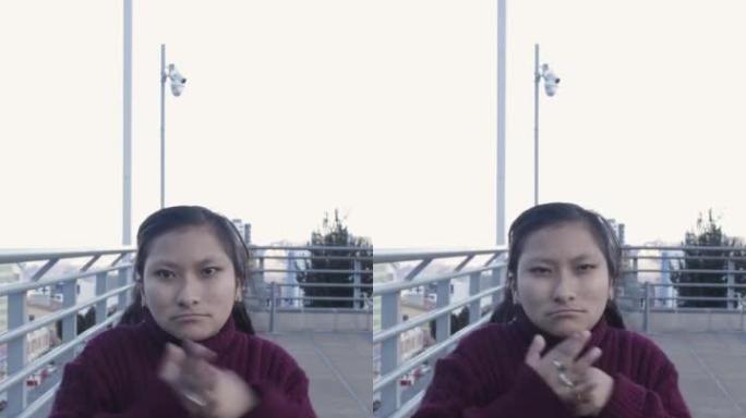 在户外，一名西班牙裔女性用愤怒的表情将拳头击中手掌的垂直镜头。