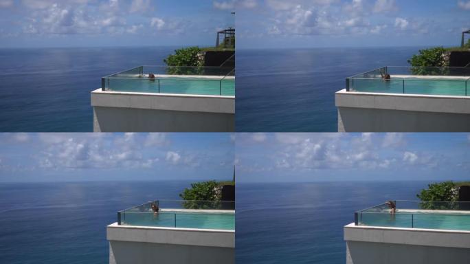 一名女子在无边泳池中游泳，俯瞰大海。她慢慢游到边缘，抓住泳池栏杆，看到隔板外面有什么。