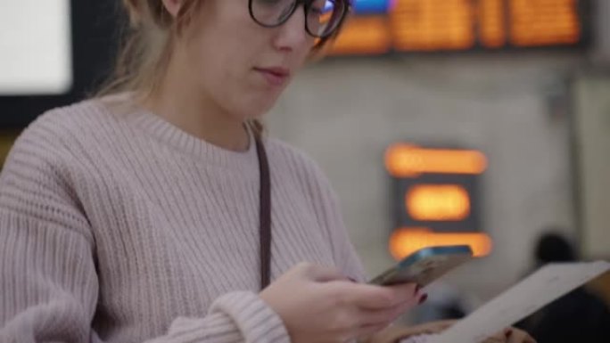 女人看着火车出发牌用手机扫描火车票上的二维码