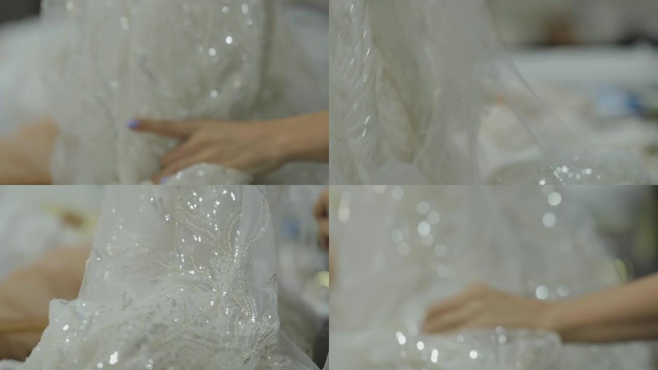 裁缝美丽的手触摸白色闪亮面料生产婚纱
