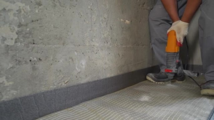 一名工人用钻头将玻璃棉固定在地板上。主人钻地板并固定隔音。在地板上安装隔音设备。