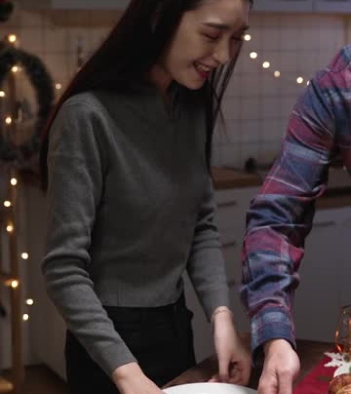 垂直屏幕: 亚洲韩国男性拿着美味的火鸡从厨房走到餐厅吃圣诞晚餐。男人在挨饿的女友时把鸡肉放在盘子上