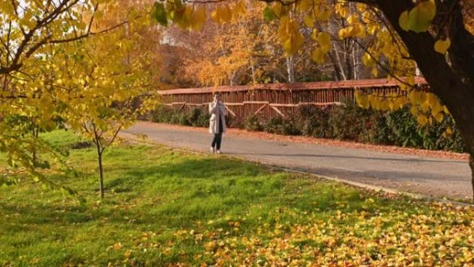 在一个秋日阳光明媚的日子里，一个穿着米色毛呢大衣的漂亮女人走在满是落叶的街道上