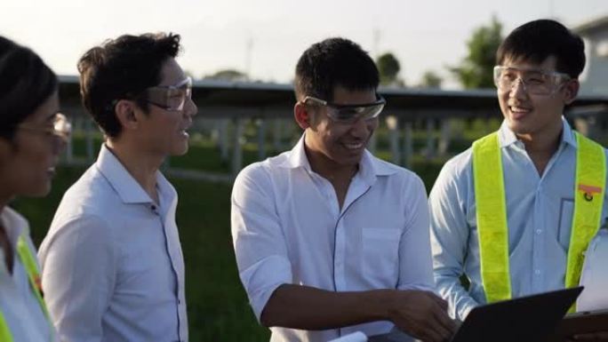背光镜头，一组亚洲工程团队在计划操作和站内光伏太阳能电池板使用笔记本电脑和平板电脑，年轻的检查员工程