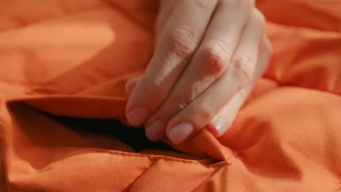 女性双手触摸摸索材料橙色防水面料冬季夹克、羽绒服。纺织、服装生产，秋季亮丽夹克。时尚，时尚。衣服背景