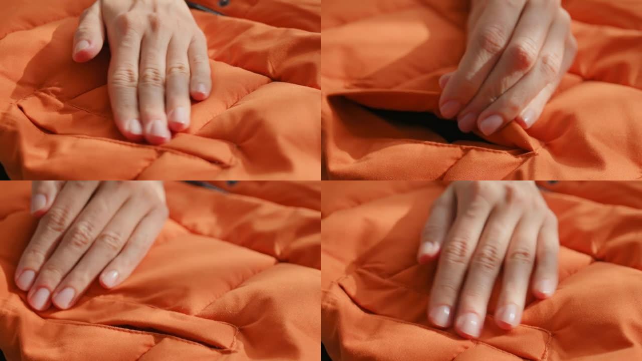 女性双手触摸摸索材料橙色防水面料冬季夹克、羽绒服。纺织、服装生产，秋季亮丽夹克。时尚，时尚。衣服背景