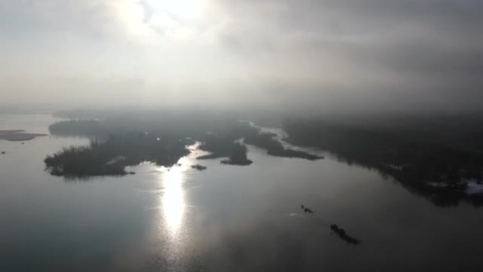 无人机在雾和云中飞过冰冻的湖面，阳光普照