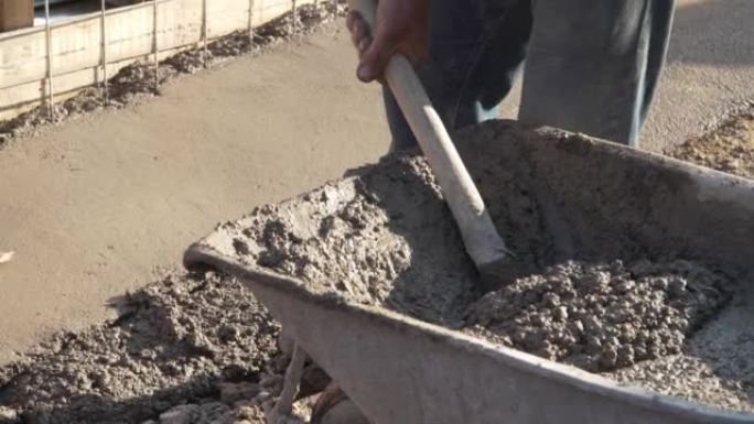 不明男子的中段手持铲子，将水泥混凝土从施工现场的手推车上放到地面建筑路面上