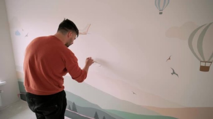 艺术家正在儿童房里用图画装饰墙壁。新房子墙壁的艺术画。维修工程。