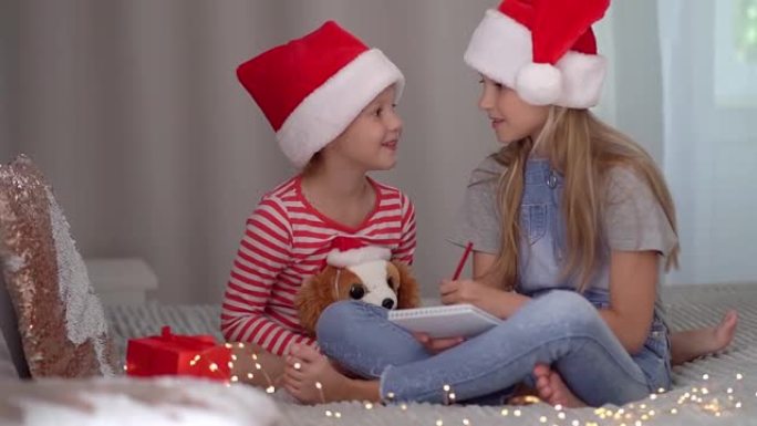 戴着红色圣诞帽的两个姐妹女孩给圣诞老人写了一封信