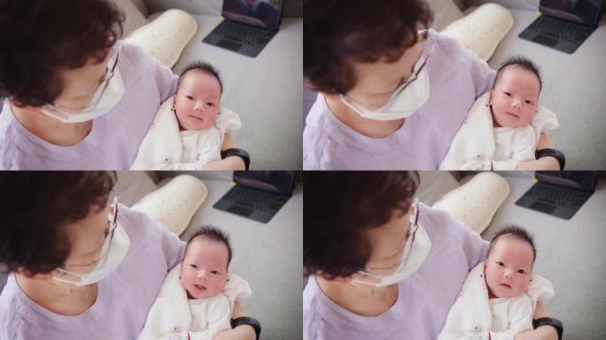 快乐的亚洲祖母戴着防护面具说话看着孙女刚出生的婴儿在祖母舒适的怀里在家，退休的祖父母照顾孙子，童年