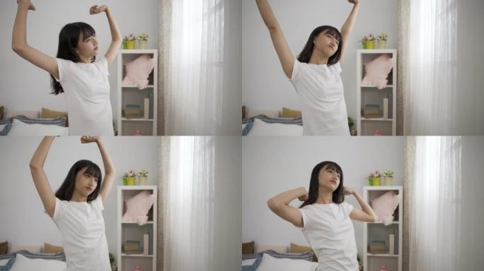 早上起床后，在现代明亮的室内装饰中，一个精神焕发的亚洲女孩站在窗户附近，伸着双手