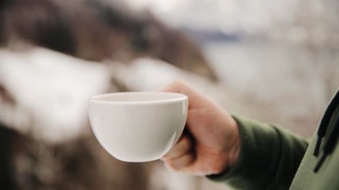 男人旅行者享受咖啡时间的风景，在模糊的背景下可以看到山和薄雾的早晨。冬季男性手捧杯热饮