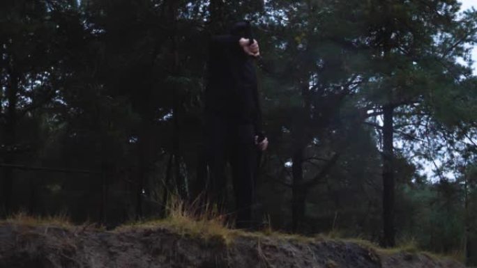 黄昏时分，在悬崖边上，一个穿着黑色衣服的男人以慢动作拿出武士刀。在森林的背景下，一个穿着忍者服装的人