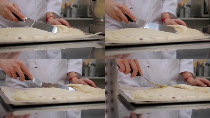 糕点厨师用刮刀将面团铺在烤盘中的特写镜头。