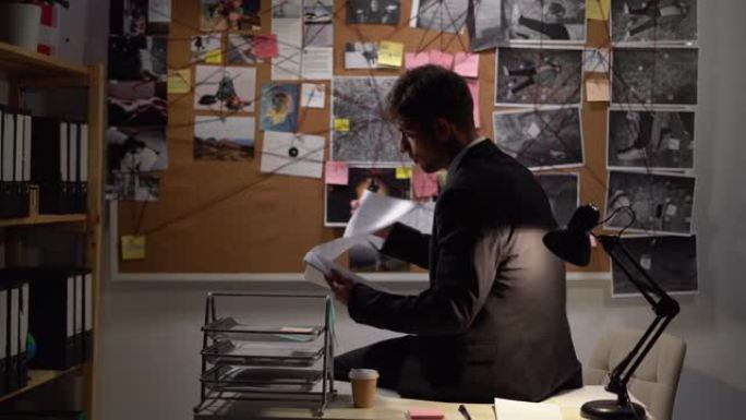 侦探看着办公室里有照片的证据板，晚上工作