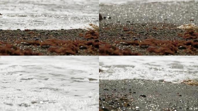 海卵石和海藻扔在岸上。一浪正好冲入框架。岩石上的眩光。用三脚架拍摄的长镜头