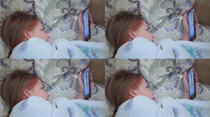 一个年轻女孩躺在床上，上床睡觉前在智能手机上的社交网络上观看视频。