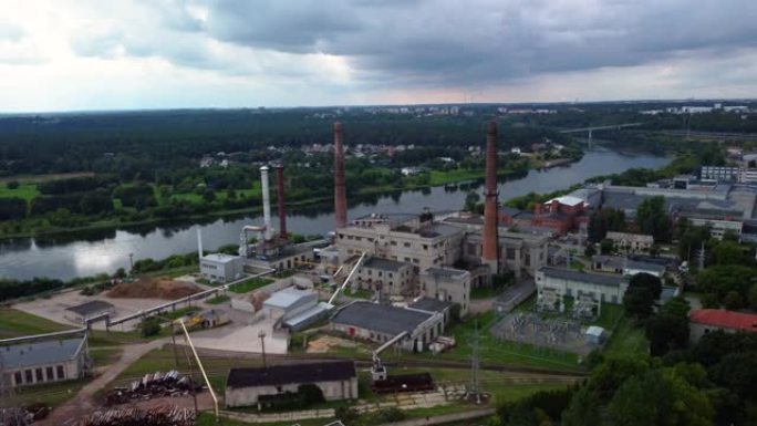 在树木和多云的天空的背景下，沿河的工厂和建筑物的4k航拍画面