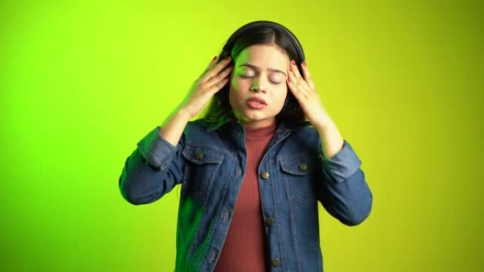 美丽的年轻女子用耳机听音乐，亚洲印度女孩摘下耳机避免大声音乐，耳朵疼痛概念，孤立的彩色背景工作室拍摄