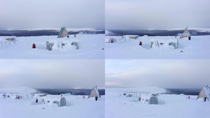 冬天在直升机上沿着山区避难所飞行，雪地里有房子，还有站立的滑雪板