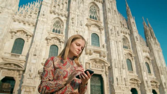 女人在夏日在意大利米兰的地标大教堂附近使用智能手机应用程序