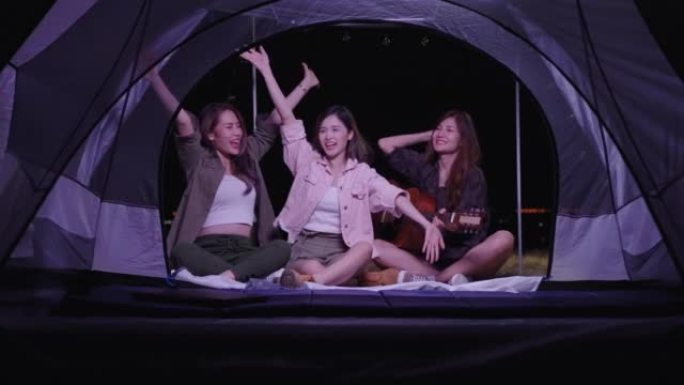 一群年轻的亚洲朋友在暑假露营期间在帐篷里弹吉他和唱歌。自由、休闲、旅行、冒险的概念
