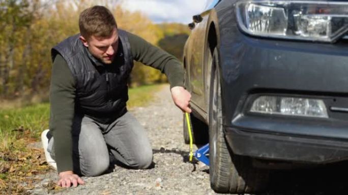 男子将汽车举在千斤顶上，以更换被刺破的轮胎。更换道路上的轮胎。帮助