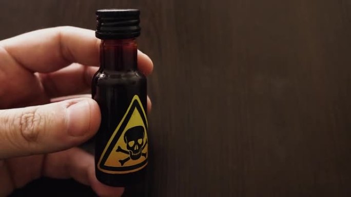 手拿着一小瓶带有黄色毒性标志的毒药，由头骨和两块骨头图标表示-危险的混合物或冲泡中毒，以饮用或注射