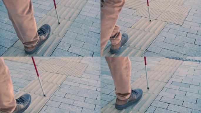 盲人在直的触觉瓷砖上使用白色手杖来导航道路
