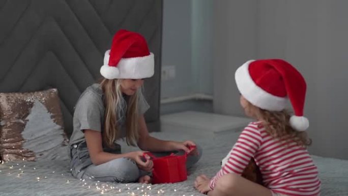 一个戴着圣诞老人帽子的女孩在圣诞节的红色盒子里给她的妹妹女朋友送礼物