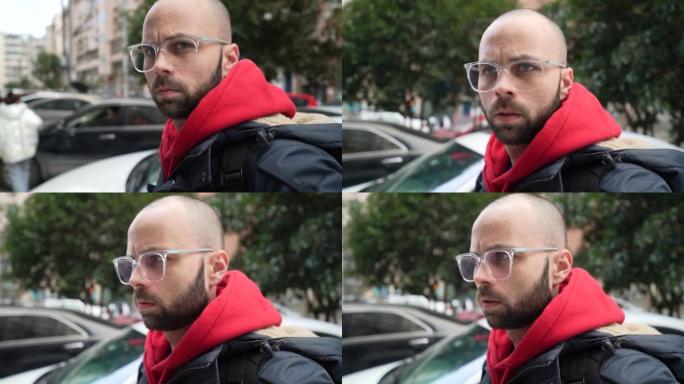 一个白人男性戴着眼镜，胡须和浅色头发站在街上的特写镜头