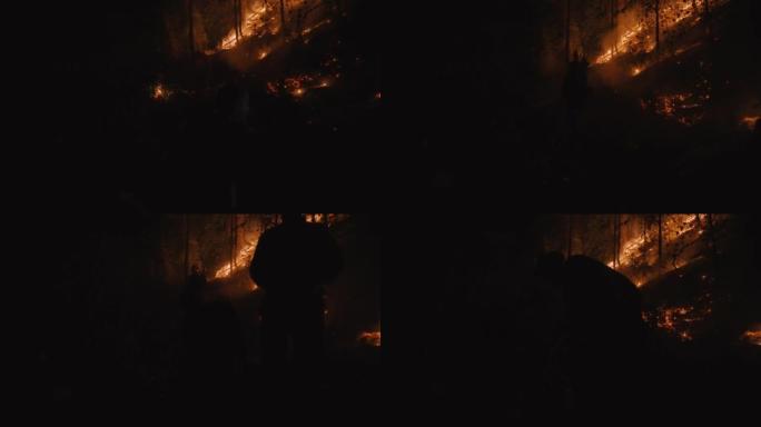 戏剧性和极端的肩膀POV消防员剪影在黑暗的夜晚，因为他们与山坡野火战斗